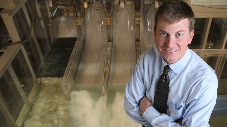A man stands in front of a hydraulic laboratory model