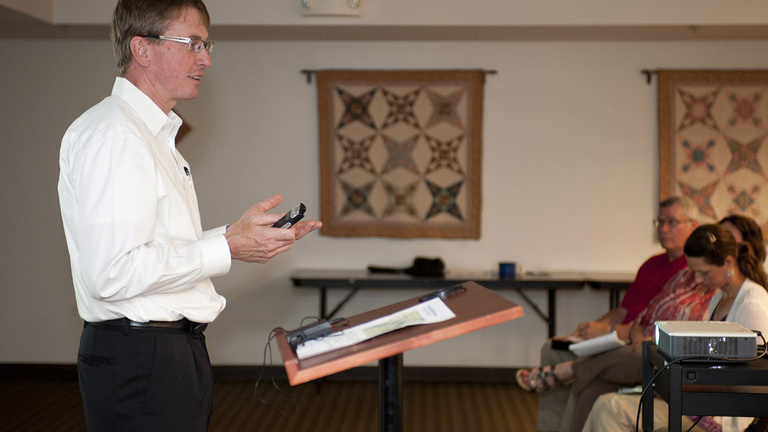A man stands in the front of a classroom, speaking to a group of people